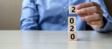 İş adamı elinde ahşap bir küp tutuyor ve masa da 2020 kelime var.