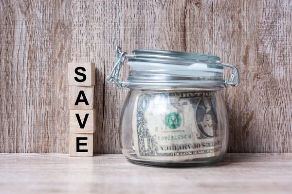 Bloco de madeira com texto SAVE e dinheiro dólar americano em frasco de vidro — Fotografia de Stock