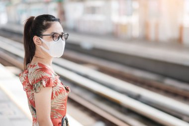 Surat maskesi takan genç bir Asyalı kadın, tren istasyonunda koronavirüs dönüşümünü koruyor. Sosyal uzaklık, yeni normal ve covid-19 salgınından sonraki yaşam