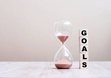 Masanın üzerinde GoALS tahta küp blokları olan kum saati geçen zamanı ölçen kum saati ampulü içinden akıyor. Geri sayım, teslim tarihi, yaşam süresi ve emeklilik kavramı