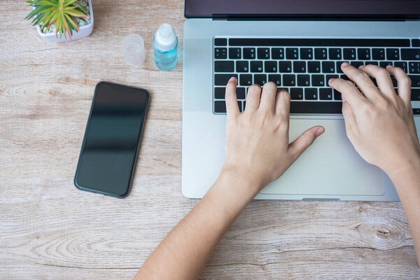 Женщина, использующая ноутбук и смартфон во время работы дома с дезинфицирующим спиртом для защиты коронавируса (Covid-19) инфекции. Новая концепция нормальной, личной истерики и чистой поверхности
