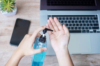 Evde çalışırken iş yerinde el temizleyicisi ve akıllı telefon cihazları ile el temizleyen kadın, Coronavirus (Covid-19) enfeksiyonu. Kişisel hijyen ve Yeni Normal kavramı