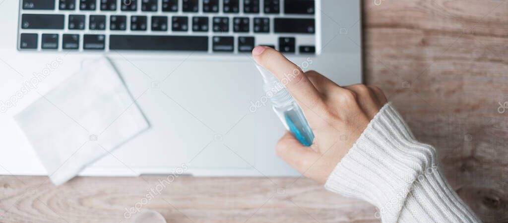 Woman cleaning laptop by wet wipes tissue and alcohol disinfectant on workplace during working and online learning at home office, protection coronavirus (Covid-19) infection. New Normal concept
