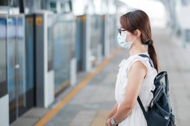 Surat maskesi takan genç bir Asyalı kadın, tren istasyonunda koronavirüs dönüşümünü koruyor. Sosyal uzaklık, yeni normal ve covid-19 salgınından sonraki yaşam