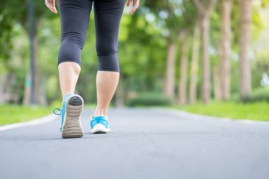 Spor ayakkabılarıyla parkta koşan genç bir kadın, sabah yolda koşan ve yürüyen bir kadın, sporcunun bacak kasları. Egzersiz, sağlık, sağlıklı yaşam tarzı ve egzersiz kavramları.