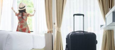 Modern otel odasında, mutlu, genç bir kadın pencereyi açıyor, Asyalı kadın turist güzel doğa manzarasına bakıyor. Seyahat, rahatlama, yolculuk, gezi ve tatil kavramları zamanı