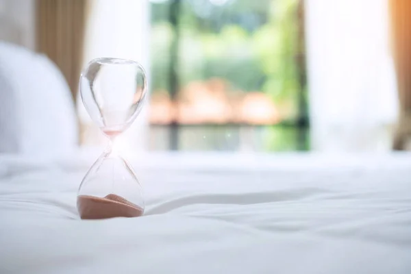 Hourglass on bed in the morning sunlight, Sand flowing through the bulb of Sandglass measuring the passing time. countdown, deadline, Life time and Retirement, daily routine concept