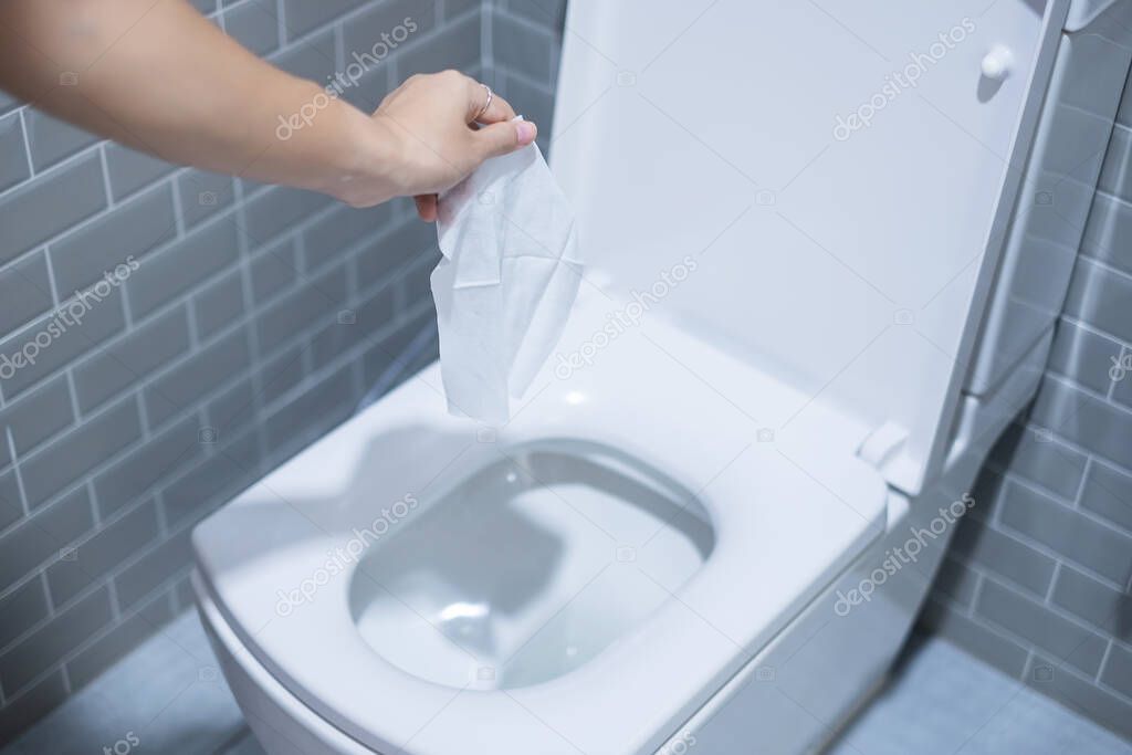 Woman hand throw paper towels in the toilet bowl. Cleaning, Lifestyle and personal hygiene concept