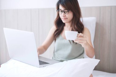 Yatak odasında yastığa dizüstü bilgisayar koyarken sıradan bir kadın kahve fincanı tutuyor. Genç yetişkin bir kadın sabah evden ya da internetten alışveriş yapıyor. Bağımsız, yaşam tarzı ve teknoloji kavramları