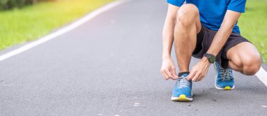 Spor kıyafetli genç bir erkek parkın dışında ayakkabı bağı bağlıyor, atlet koşucu sabahları koşuya ve koşuya hazır. Egzersiz, sağlık, sağlıklı yaşam tarzı ve egzersiz konsepti.