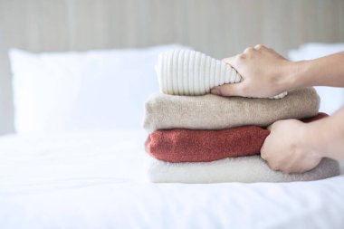 Kadın lüks bir otelde, otelde ya da evde bej rengi yün kazakları yatağa uzatıyor. Rahatla, sonbahar ya da kış giysileri, çamaşır ve tatil konseptleri