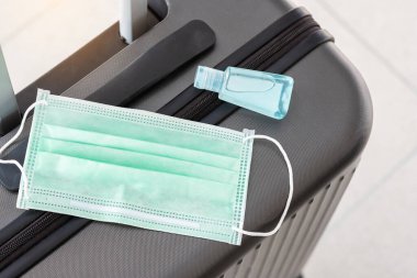 Uluslararası havaalanı terminalinde cerrahi maske ve alkol jeli el dezenfektanı bulunan bavul, Coronavirus hastalığı enfeksiyonunu koruyor. Yeni Normal ve COVID-19 kavramları altında seyahat