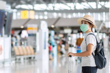 Havaalanı terminalinde yürüyen yüz maskesi takan genç bir kadın, Coronavirus hastalığını (Covid-19) koruyan, şapkalı Asyalı bir kadın gezgin. Yeni Normal ve seyahat balonu kavramı