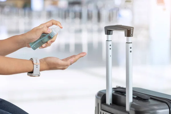 woman hand spraying alcohol sanitizer after holding handle Luggage bag in airport terminal, protection Coronavirus disease infection. New Normal, safety and travel transport under COVID-19 concepts