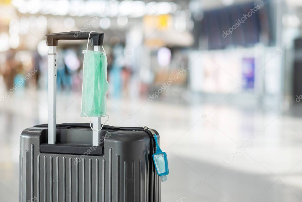 Luggage bag with surgical face mask and alcohol gel hand sanitizer in international airport terminal, protection Coronavirus disease (Covid-19) infection. New Normal and travel bubble concepts