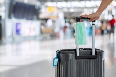Uluslararası havaalanı terminalinde cerrahi maske ve alkol jeli el dezenfektanı bulunan bavul, Coronavirus hastalığı (Covid-19) enfeksiyonunu koruyor. Yeni Normal ve seyahat balonu kavramları
