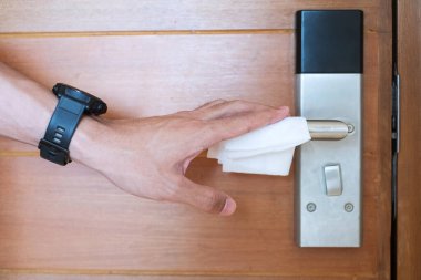 İnsan eliyle dijital kapı kulpu ıslak mendil, koronavirüs ya da Corona Virüs Hastalığı (Covid-19) ile kamu odasında temizlenir. Temiz yüzey, yaşam tarzı, güvenlik seyahati ve yeni normal kavram