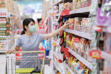 Koruyucu yüz maskesi takan ve marketten ya da mağazadan alışveriş yapan genç bir kadın koronavirüsü korur. Sosyal uzaklık, yeni normal ve covid-19 salgını altında yaşam