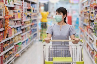 Koruyucu yüz maskesi takan ve marketten ya da mağazadan alışveriş yapan genç bir kadın koronavirüsü korur. Sosyal uzaklık, yeni normal ve covid-19 salgını altında yaşam