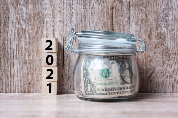 2021 Happy New Year with US dollar money glass American on wood table background. business, investment, retirement planning, finance, Saving and New Year Resolution concepts