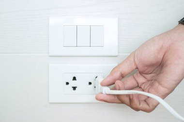 Erkek parmağının fişten çekilmesi ya da evdeki beyaz duvara elektrik cihazı takılması. Enerji tasarrufu, güç, elektrik ve yaşam tarzı kavramları