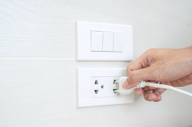 Erkek parmağının fişten çekilmesi ya da evdeki beyaz duvara elektrik cihazı takılması. Enerji tasarrufu, güç, elektrik ve yaşam tarzı kavramları