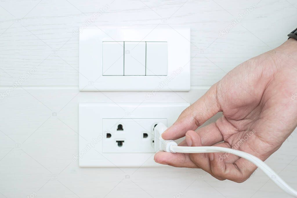 Closeup Male finger unplugging or plugging of electricity device on white wall at home. Energy Saving, power, electrical and lifestyle concepts