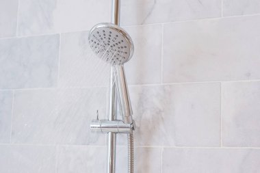 Su damlaları duş başlığı ve musluktan akıyor ve modern banyoda mermer duvar arkaplanı var.