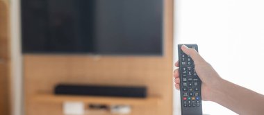 Ev veya lüks oteldeki modern odadaki Smart TV 'yi ayarlamak için uzaktan kumanda kullanılıyor.