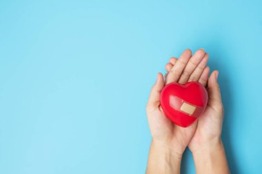 Kırmızı kalbi mavi arka planda tutan kadın. Sağlık, hayat sigortası, sağlık ve Dünya Kalp Günü konsepti