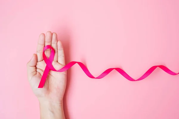 October Breast Cancer Awareness month, adult Woman hand holding Pink Ribbon on pink background for supporting people living and illness. International Women, Mother and World cancer day concept
