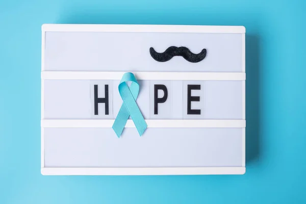 Prostate Cancer Awareness month, Light blue Ribbon with mustache on lightbox with Hope text background for supporting people living and illness. International Men day and World cancer day concept