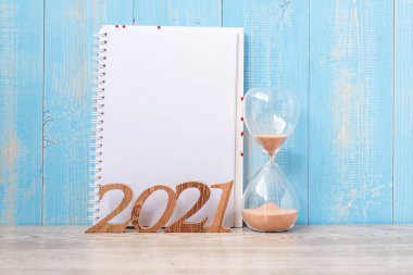 Boş not defteri, kum saati ve ahşap numarayla 2021 mutlu yıllar. Geri sayım, Yeni Başlangıç, Çözüm, Hedefler, Plan, Eylem ve Görev Konsepti