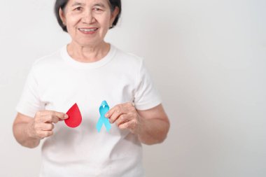 Dünya Diyabet Günü için mavi kurdeleli ve kırmızı kan damlası olan yaşlı kadın, Mavi Kasım Sağlık, Prostat Kanseri Farkındalığı, Kan şekeri kontrolü, insülin, glikoz taraması, bağış ve sağlık kontrolü