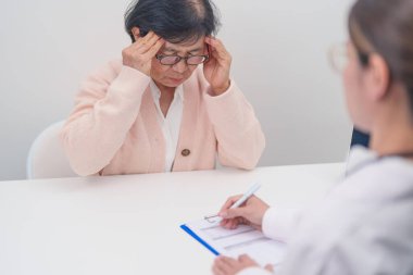 Kıdemli kadın baş ağrısı çekiyor ve bir hastalığa danışmanlık yapıyor. Yaşlı sağlık hastası, Tıbbi Teşhis, Migren, Beyin Tümörü, Beyin Felci, Bunama, Nörolojik Bozukluk, Alzheimer, Parkinson