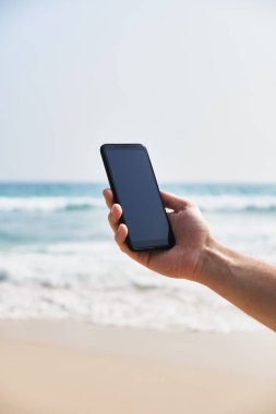 Plaj ve okyanus arka plan üzerinde erkek elinde cep telefonu.