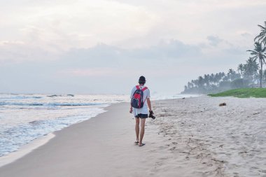 Genç bir adam sahilde yürüyor ve fotoğraf çeker.