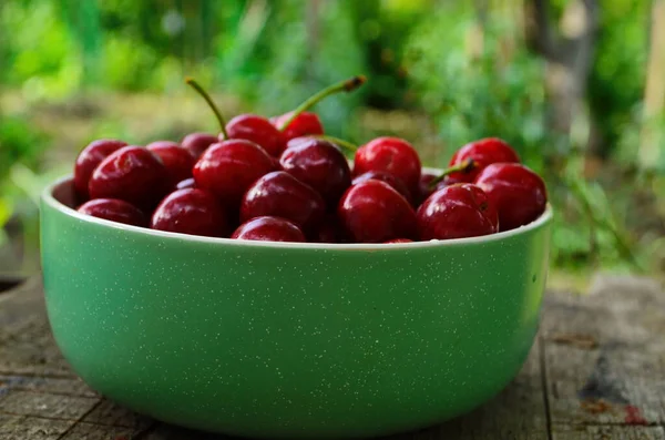 Красные спелые вишни в зеленой тарелке в саду — стоковое фото