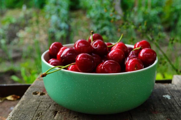 Röda mogna körsbär i en grön tallrik i trädgården — Stockfoto