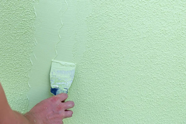 Contractor worker hand without one finger holding spatula for plaster and applying to wet concrete panted in green. Disability of worker concept.