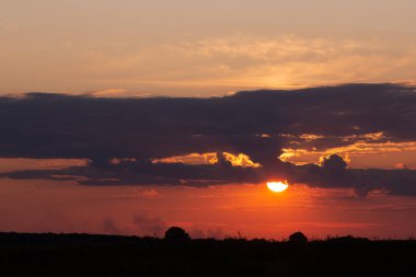 Kırsal alanda gün batımı. Fırtına bulutlarından parlayan güneş b