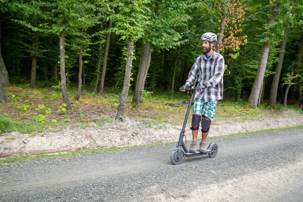 Hipster man in protective wear riding an electric scooter by a r — Stock Photo, Image