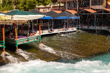 Alanya, Türkiye - 23 Haziran 2019: İnsanlar Dim nehri, Alanya, Antalya, Türkiye 'de doğrudan nehre inşa edilen gıda ve doğal su havzası ile dinlenme tesisinde dinleniyor. 