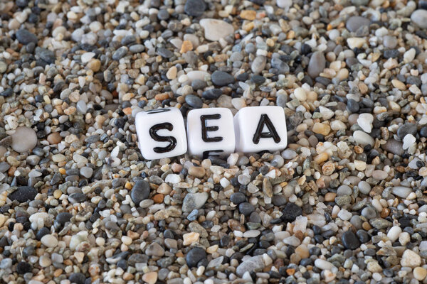 Sea inscription text in a still life of the letters layed out on a shore sand stones