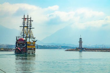 Alanya, Türkiye - 28 Ağustos 2020: Vikingen adlı turizm gemisiyle kıyı şeridi rıhtımdan bulutlarla kaplı bir deniz fenerinin yakınına geliyor. Antalia eğlence sezonu bu yıl