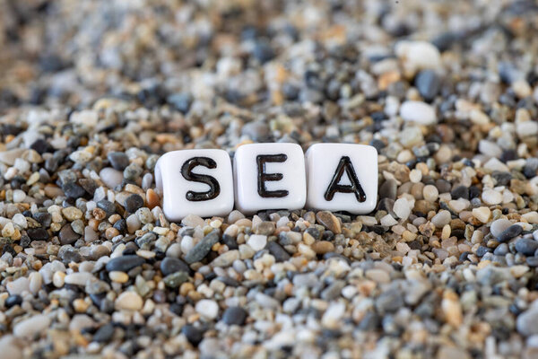 SEA inscription text in a still life of the letters layed out on a shore sand stones