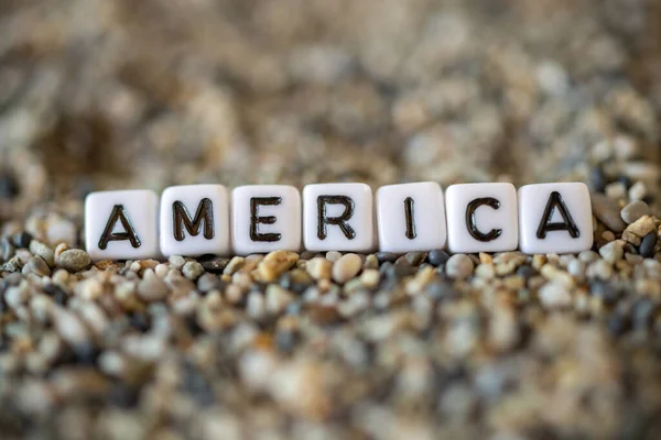 America inscription text with name of the vacation destination city in a still life of the letters layed out on a shore sand stones