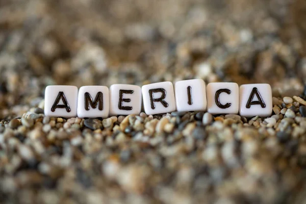 America inscription text with name of the vacation destination city in a still life of the letters layed out on a shore sand stones