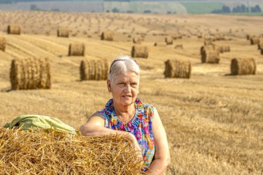 Sahada saman balyalarıyla güneş ışığının tadını çıkaran mutlu, aktif bir son sınıf kadını. Otantik çiftlik serisi