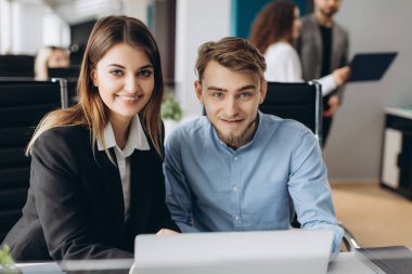 İş erkek ve kadın kameraya bakarak ve bilgisayarla çalışma çalışma masası, bir kadeh. Birlikte çalışma office iş takım odaklı.